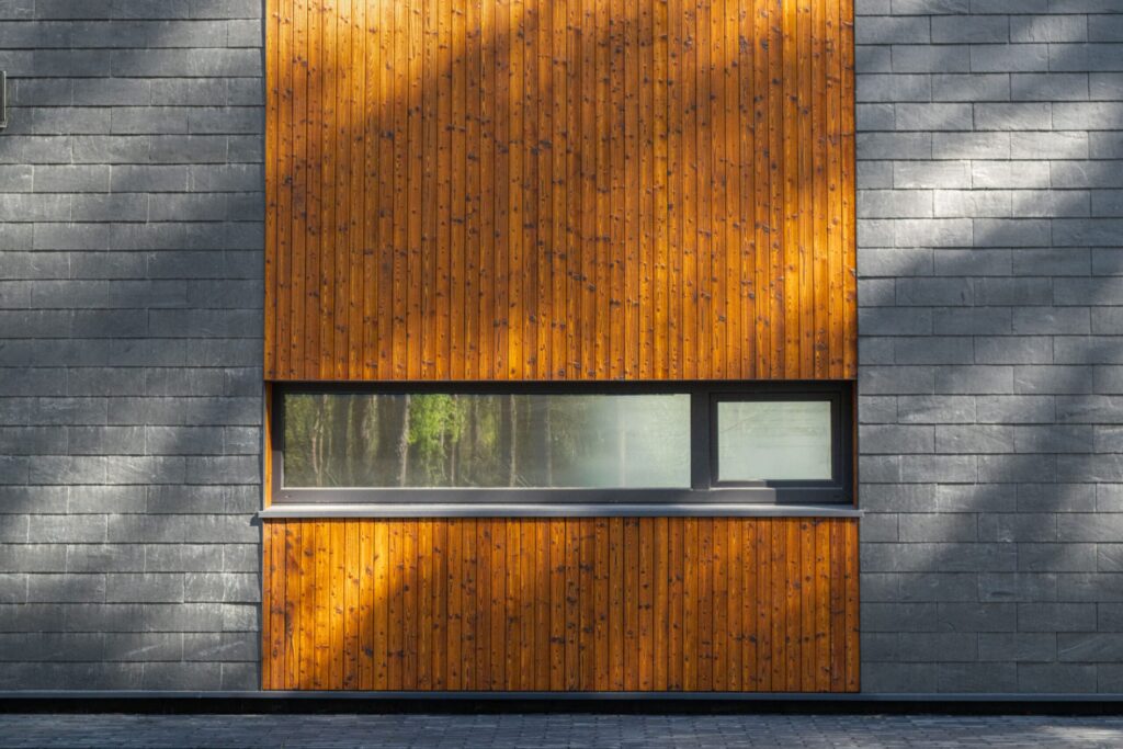 Vertically charred spruce siding on the facade, set among gray shale bricks with a horizontal window